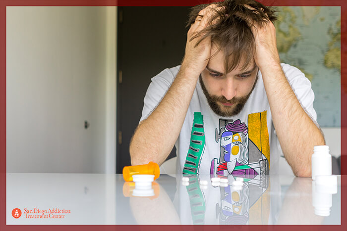 Guy sitting at a table with pills and barbiturates in front of him