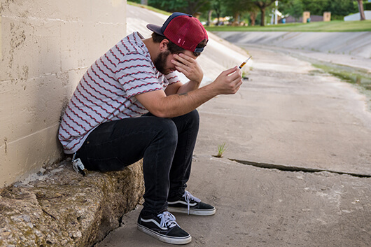 Distressed addict with needle sitting on steps