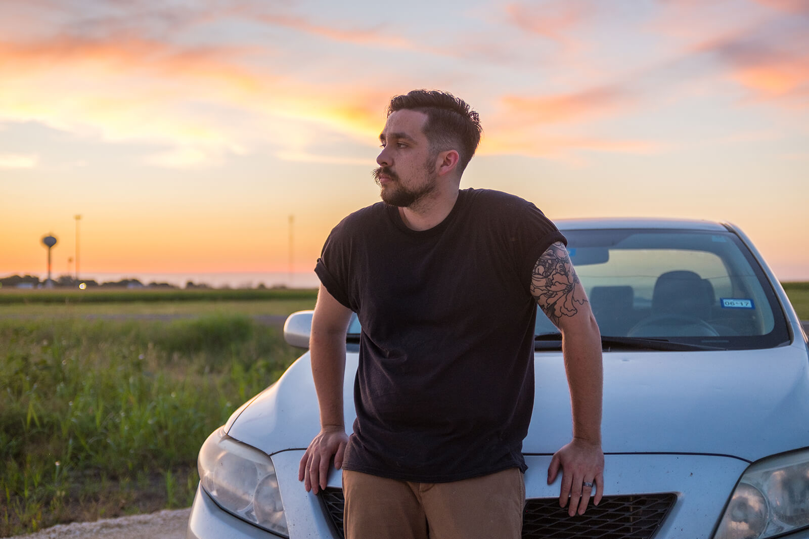 Man leaning on car with sunset in background
