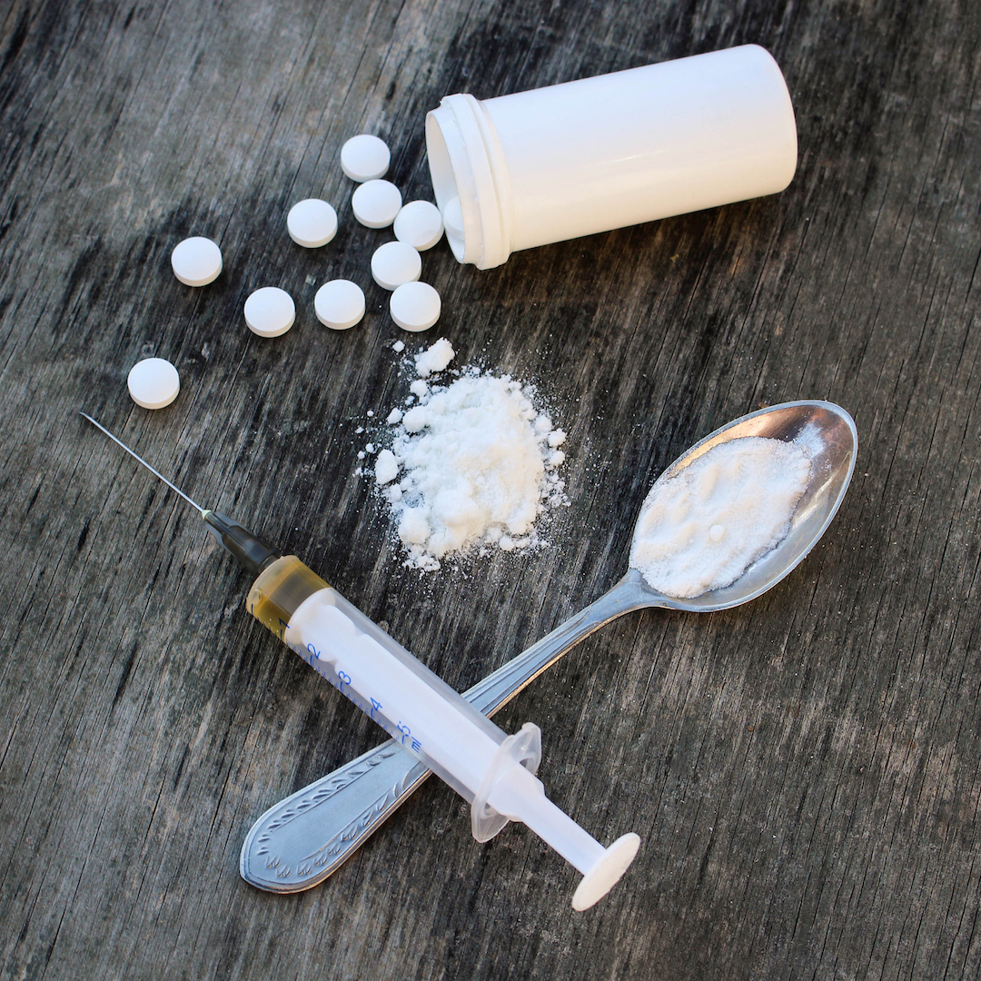 White pill, syringe and heroin on spoon on the old wooden background. Drug addiction.
